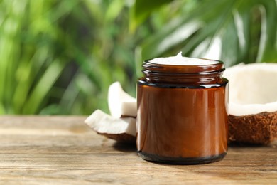 Photo of Jar of hand cream and coconut on wooden table, space for text