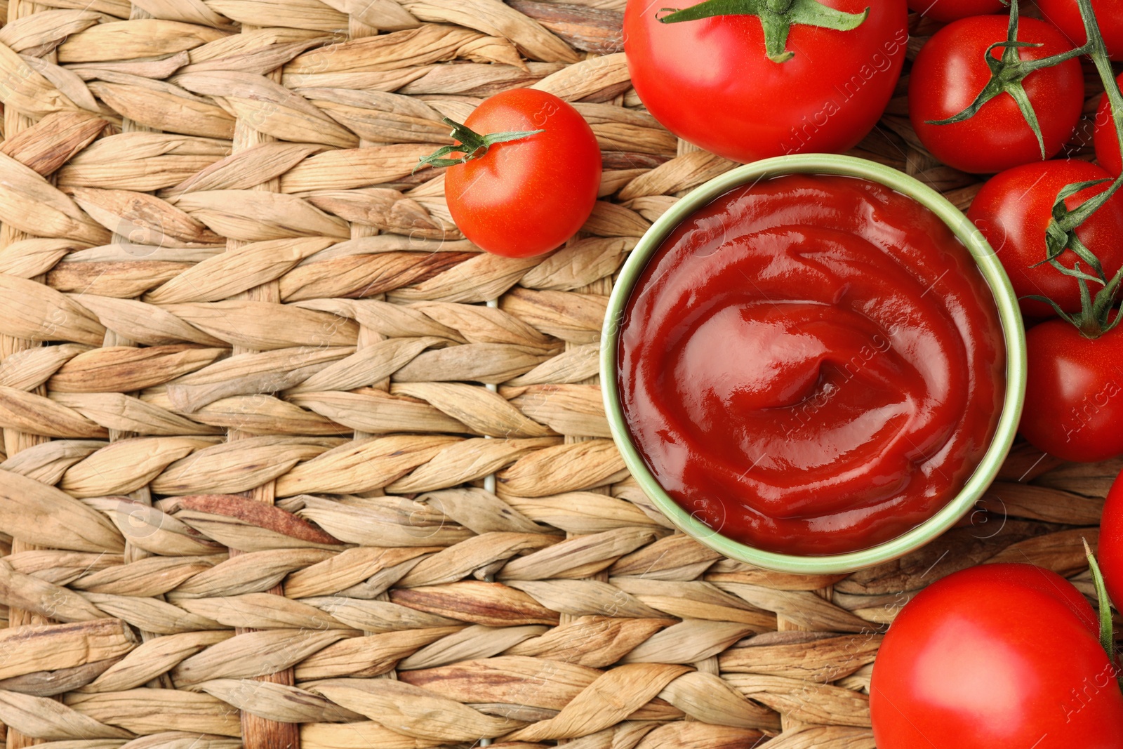 Photo of Bowl of tasty ketchup and tomatoes on wicker mat, flat lay. Space for text