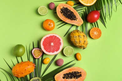 Photo of Different exotic fruits and palm leaves on green background, flat lay