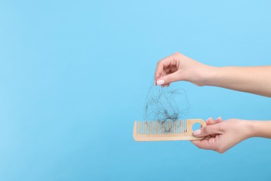 Woman untangling her lost hair from comb on light blue background, closeup and space for text. Alopecia problem