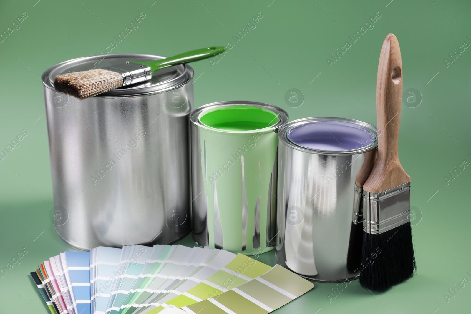 Photo of Cans of paints, palette and brushes on light green background