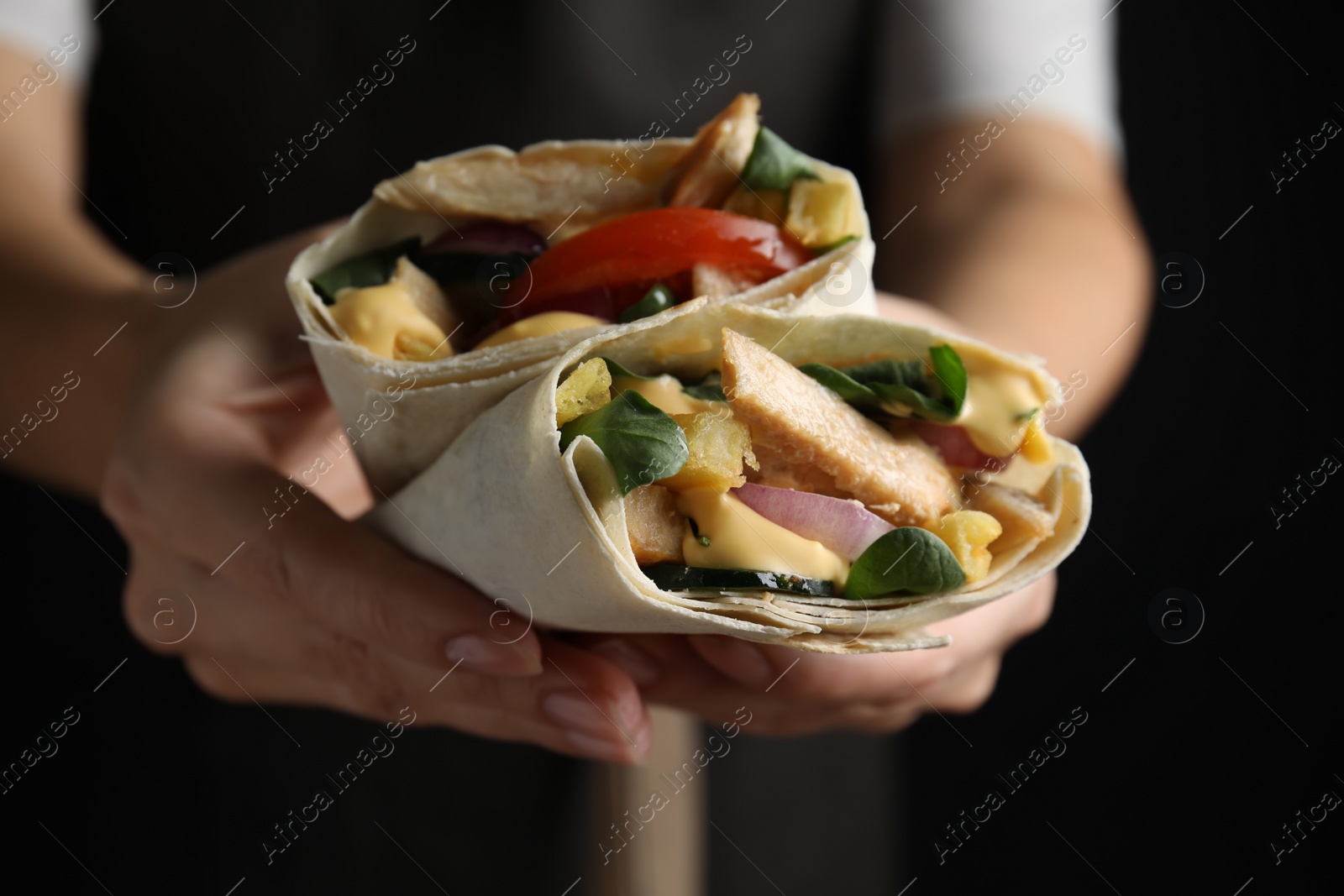 Photo of Woman holding delicious shawarmas with chicken meat and vegetables on black background, closeup