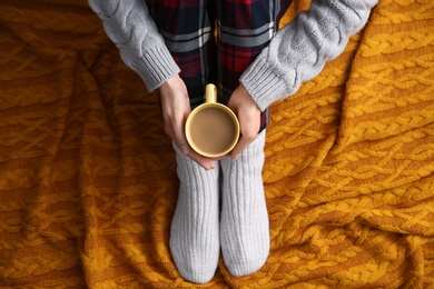 Photo of Woman relaxing with cup of hot winter drink on knitted plaid, top view. Cozy season