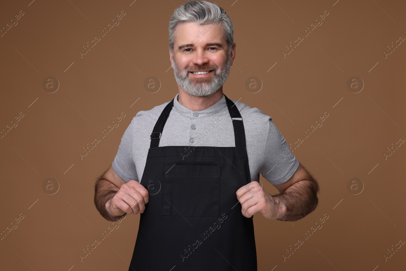 Photo of Happy man wearing kitchen apron on brown background. Mockup for design