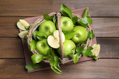 Photo of Fresh ripe green apples and leaves with wicker basket on wooden table, flat lay