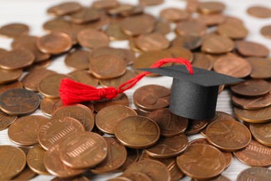 Photo of Scholarship concept. Graduation cap and coins on white wooden table, closeup