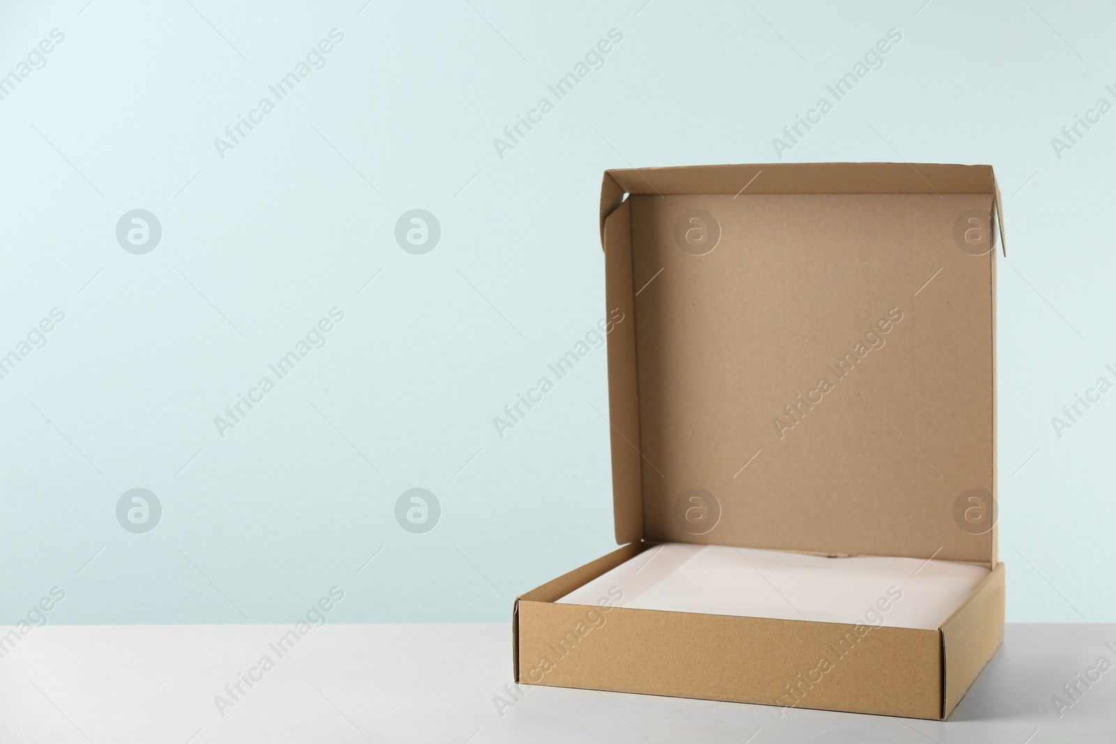 Photo of Open cardboard box on table against light background. Space for text