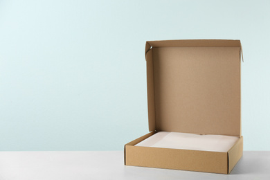 Open cardboard box on table against light background. Space for text