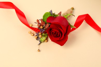 Stylish boutonniere with red rose and ribbon on beige background