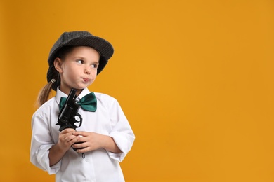 Photo of Cute little detective with revolver on yellow background. Space for text