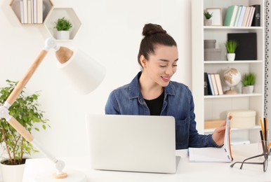 Home workplace. Happy woman looking at notebook at white desk in room