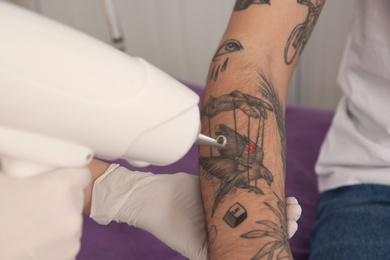 Photo of Young man undergoing laser tattoo removal procedure in salon, closeup