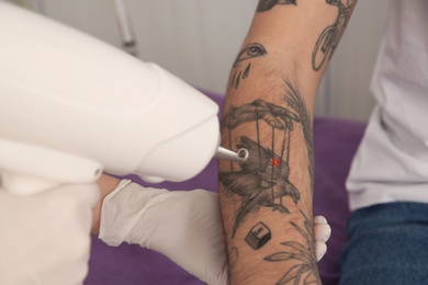 Young man undergoing laser tattoo removal procedure in salon, closeup