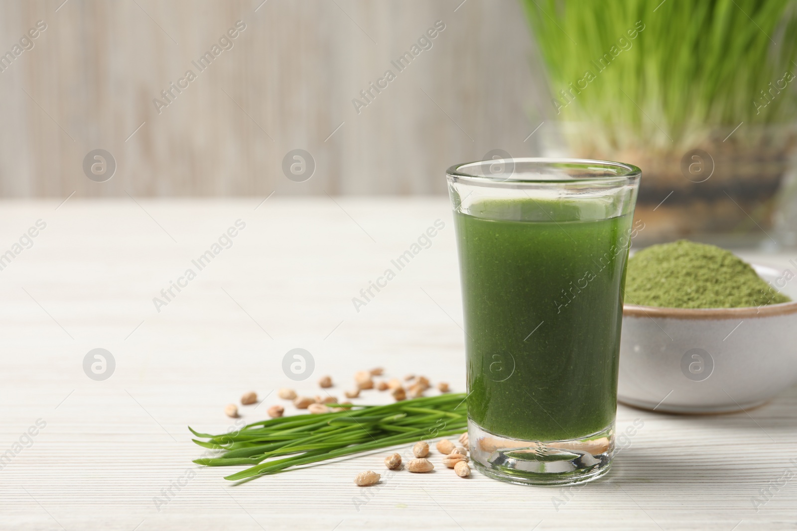 Photo of Wheat grass drink in shot glass, seeds and fresh green sprouts on white wooden table, closeup. Space for text