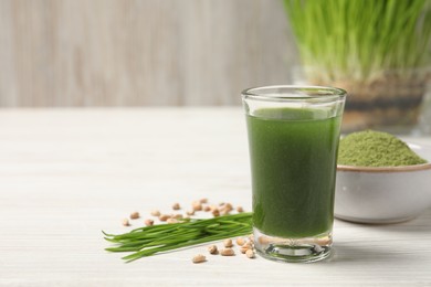 Wheat grass drink in shot glass, seeds and fresh green sprouts on white wooden table, closeup. Space for text