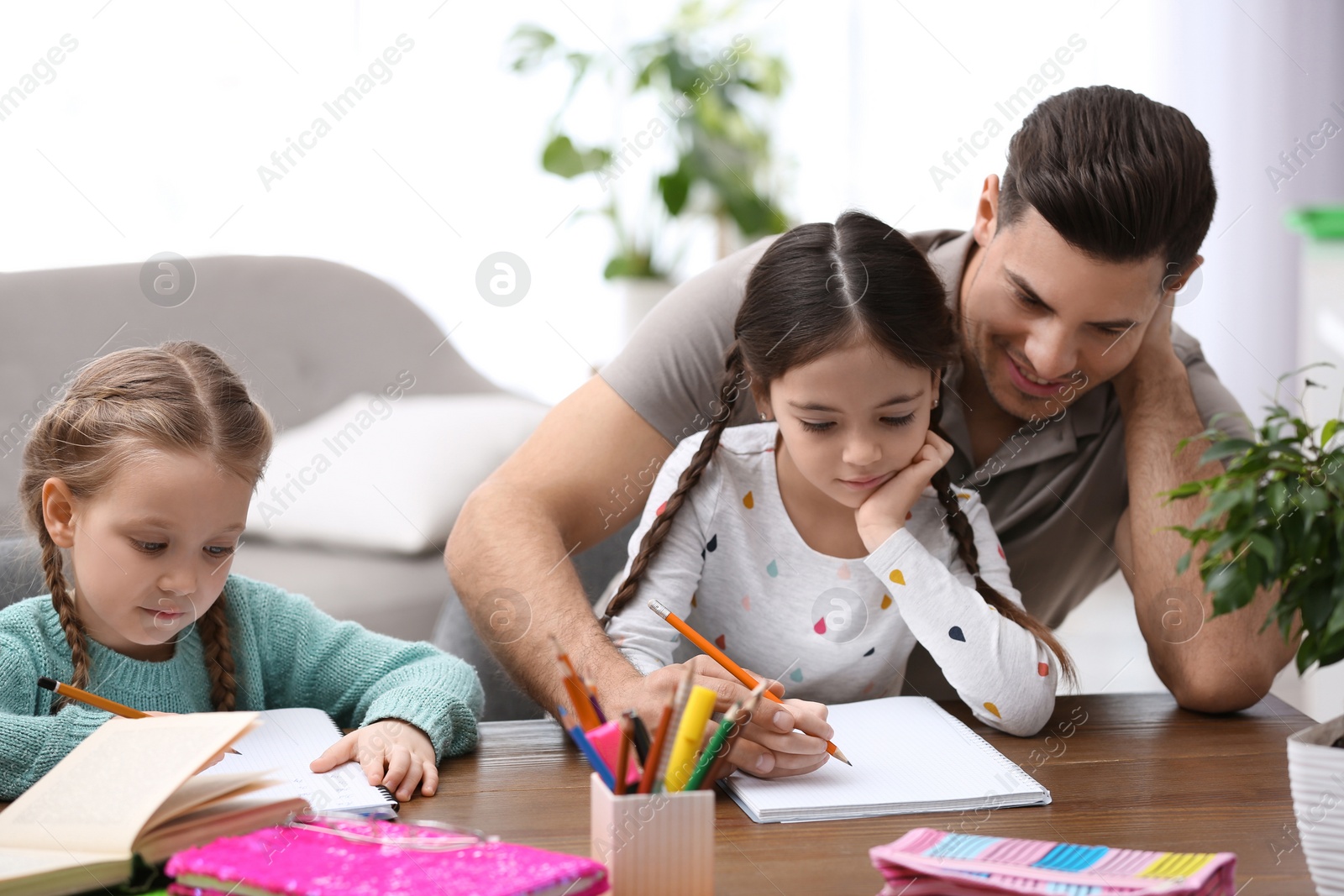 Photo of Father helping his daughters with homework at table indoors