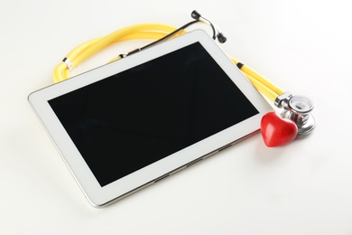 Photo of Stethoscope, tablet and small red heart on light background. Heart attack concept