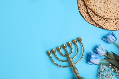 Photo of Tasty matzos, flowers and menorah on light blue background, flat lay with space for text. Passover (Pesach) celebration