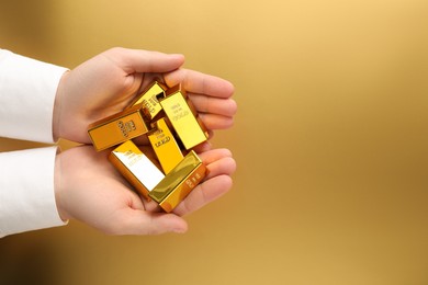 Photo of Man holding shiny gold bars on color background, top view. Space for text