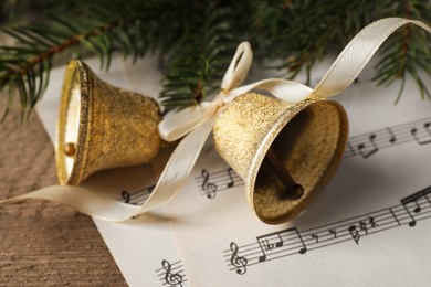 Photo of Bells, fir branches and music sheets on wooden table, closeup. Christmas decor
