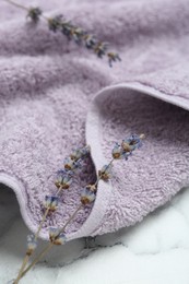 Photo of Violet terry towel and dry flowers on white marble table, closeup