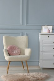Photo of Stylish armchair with pillow and chest drawers near light grey wall indoors. Interior design