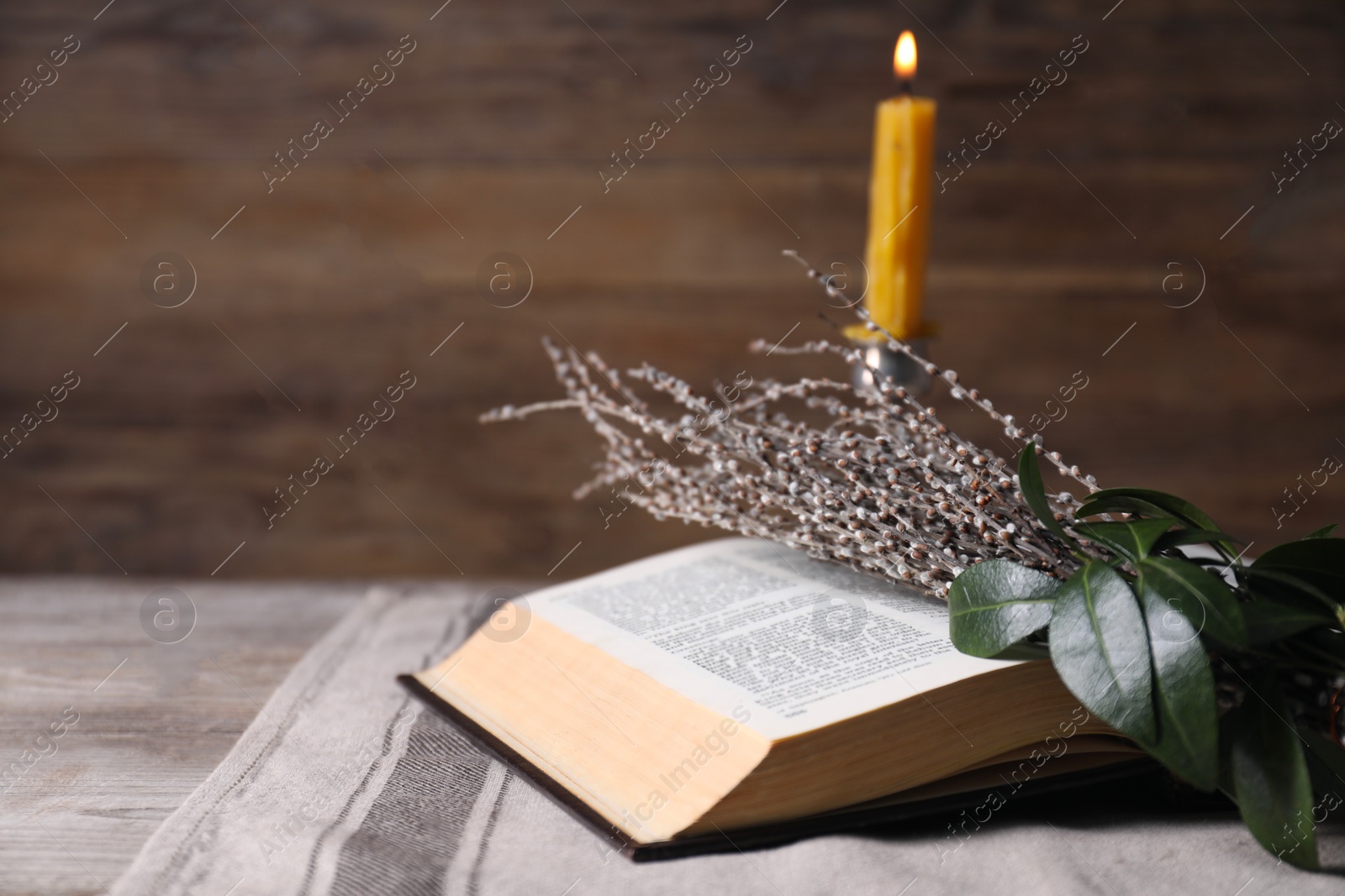 Photo of Bible, willow branches and burning candle on wooden table, closeup. Space for text