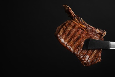 Photo of Food tongs with grilled steak and space for text on black background. Tasty meat
