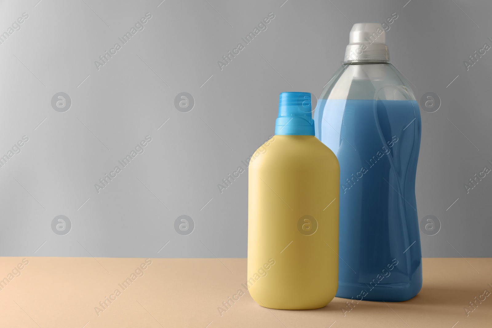 Photo of Bottles of fabric softener on pale yellow table against light grey background, space for text