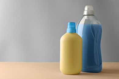 Photo of Bottles of fabric softener on pale yellow table against light grey background, space for text