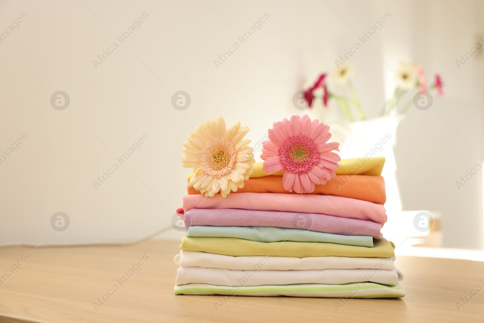 Photo of Stack of clean clothes and flowers on wooden table. Space for text