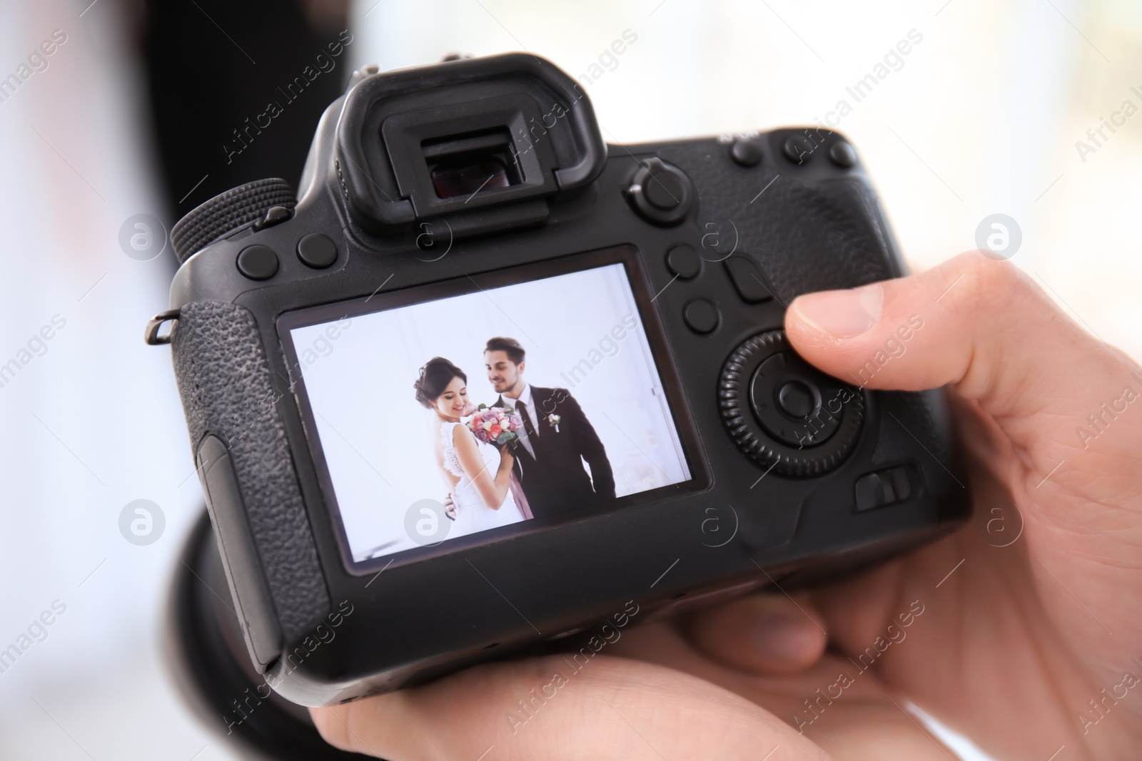 Photo of Professional photographer holding camera with lovely wedding couple on display, closeup