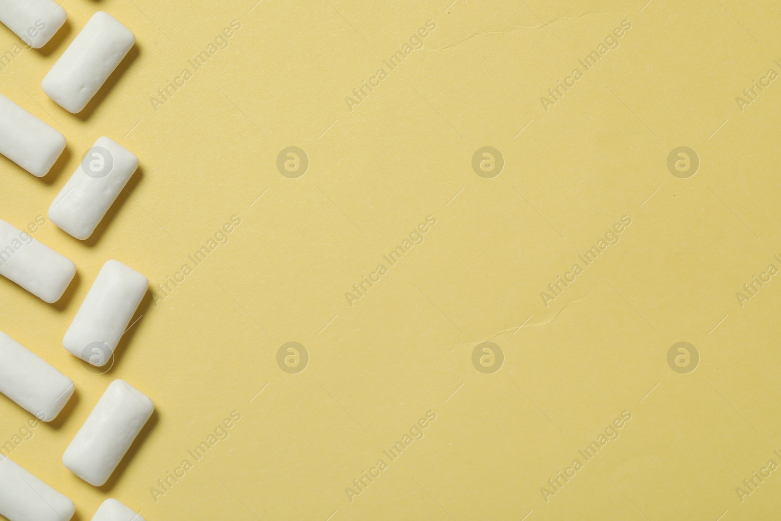 Photo of Tasty white chewing gums on yellow background, flat lay. Space for text