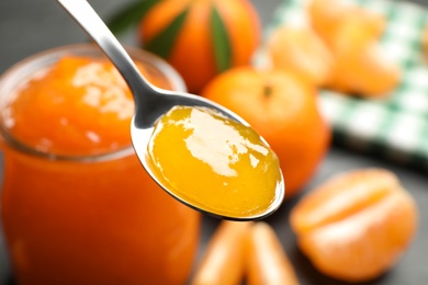 Photo of Teaspoon with tasty tangerine jam over table, closeup