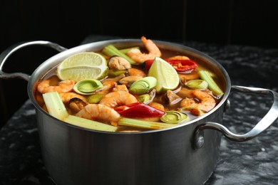 Photo of Saucepan with delicious Tom Yum soup on black marble table, closeup