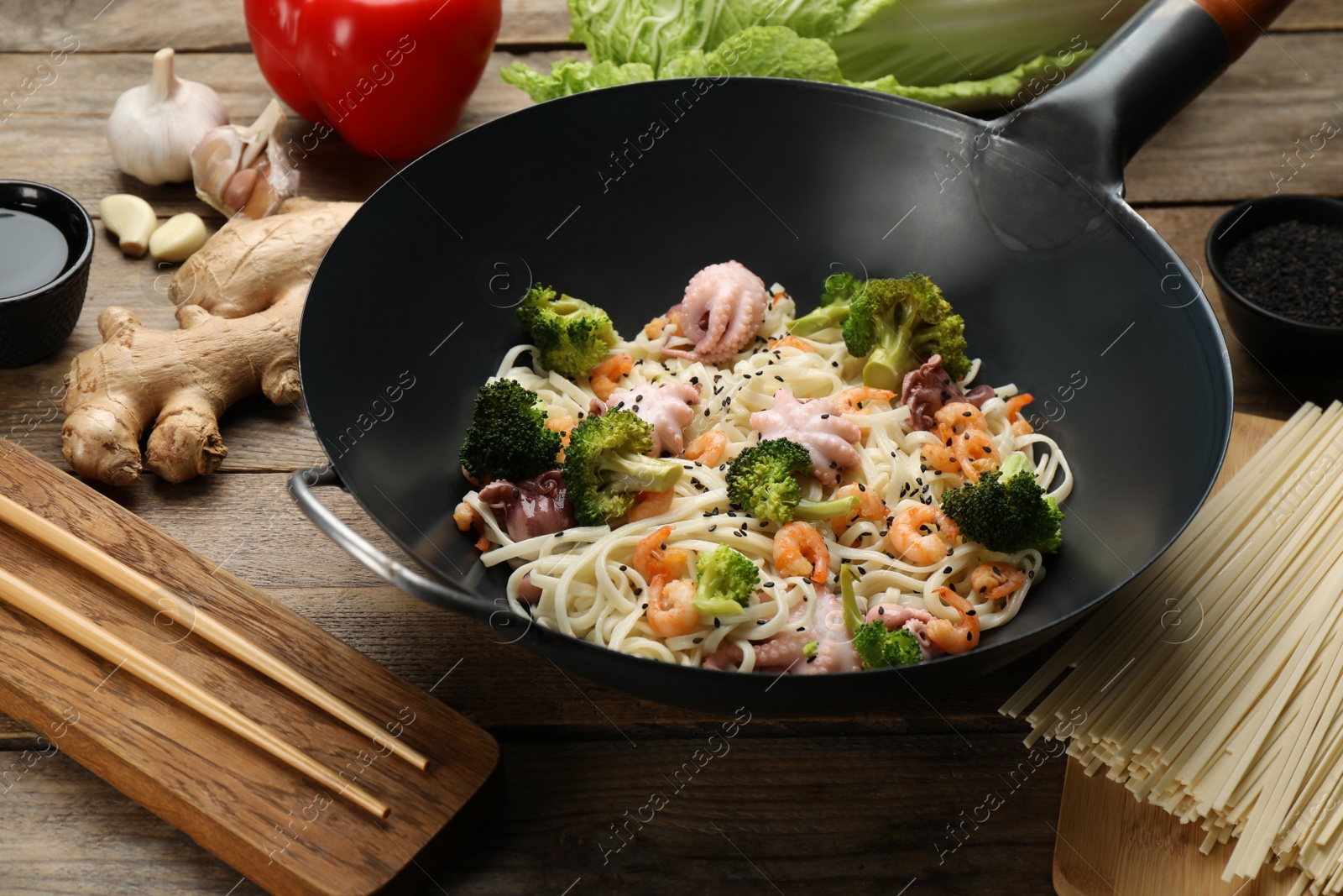 Photo of Stir fried noodles with seafood and vegetables in wok on wooden table