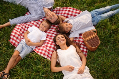 Photo of Happy family lying on picnic blanket in park, above view