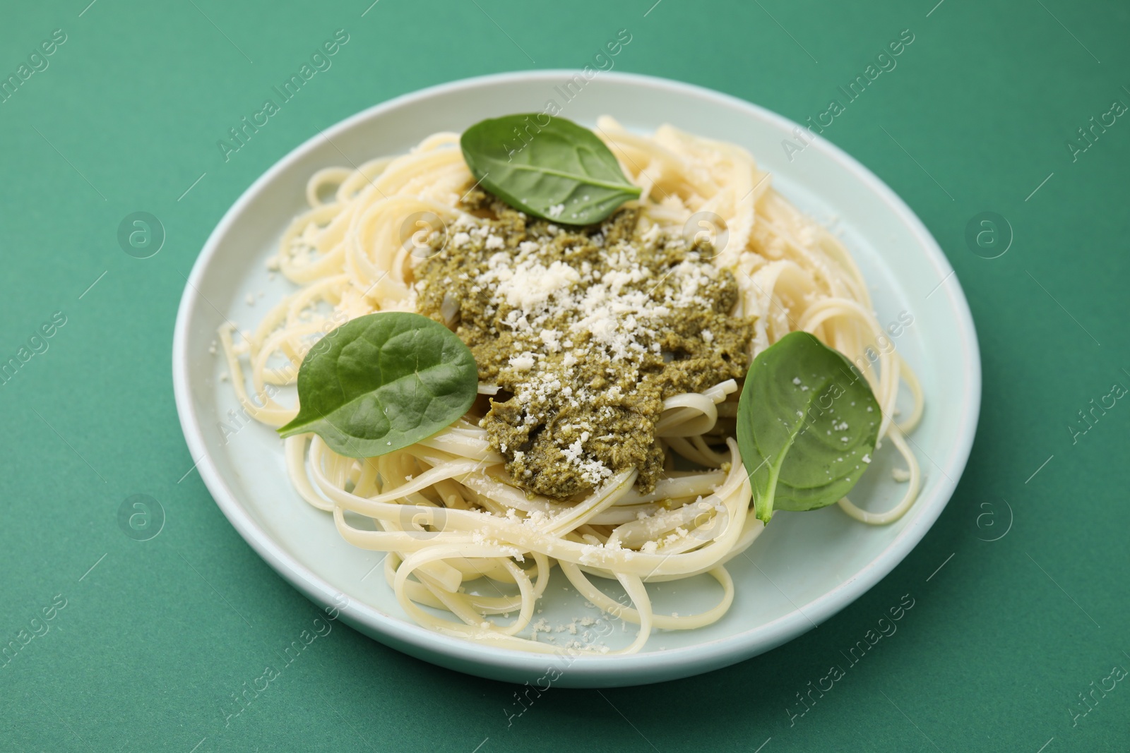 Photo of Tasty pasta with spinach, cheese and sauce on green table