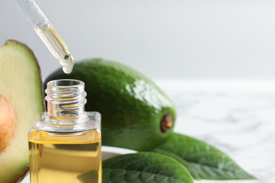 Photo of Dripping avocado essential oil into bottle on table, closeup. Space for text