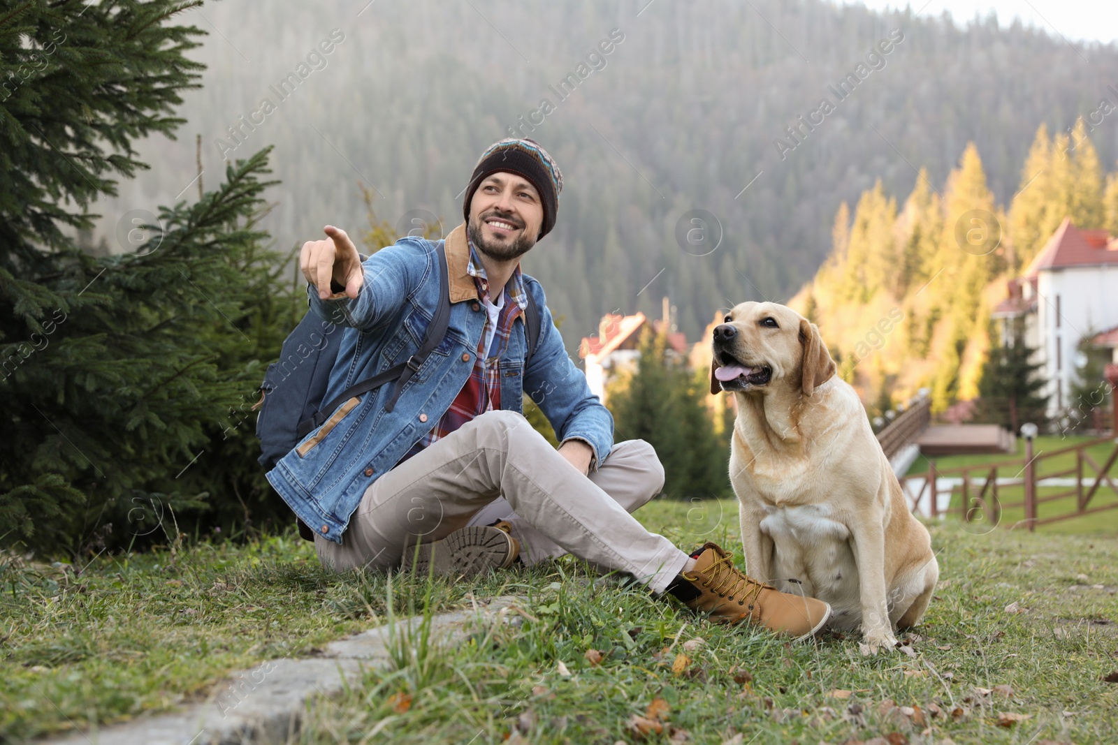 Photo of Happy man and adorable dog sitting on green grass in mountains. Traveling with pet