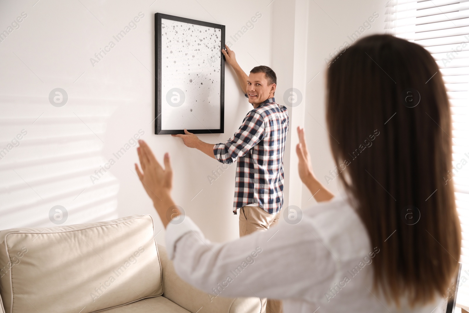 Photo of Happy couple decorating room with picture together. Interior design