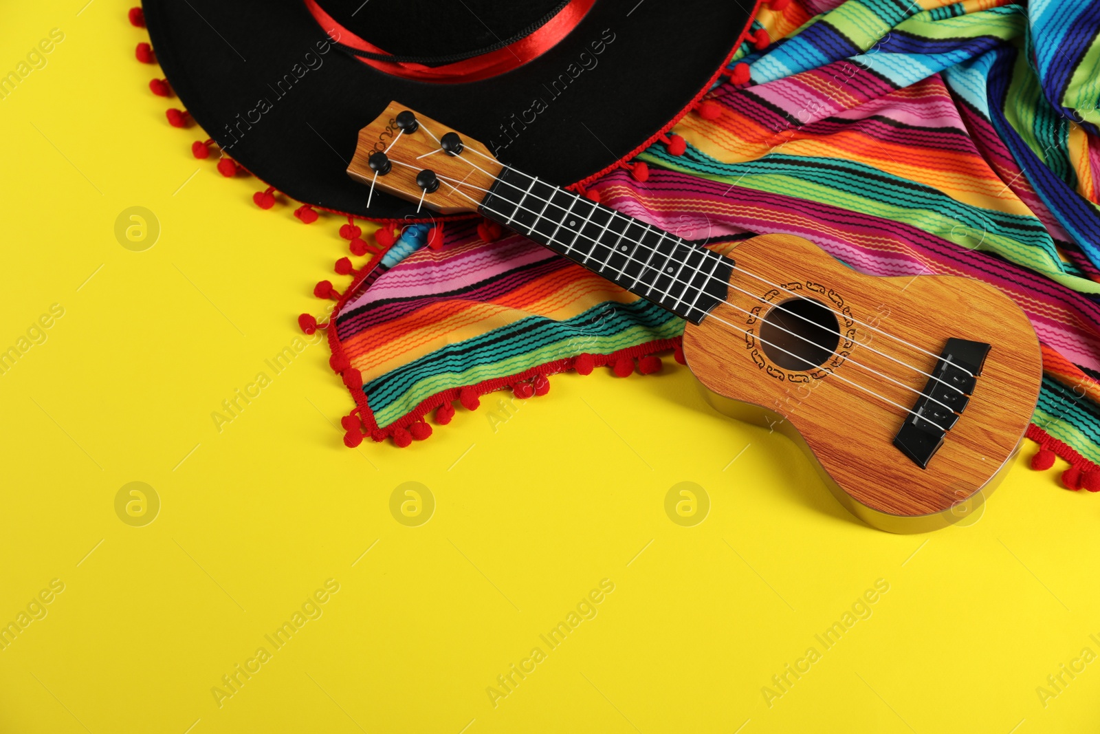 Photo of Black Flamenco hat, poncho and ukulele on yellow table, above view. Space for text