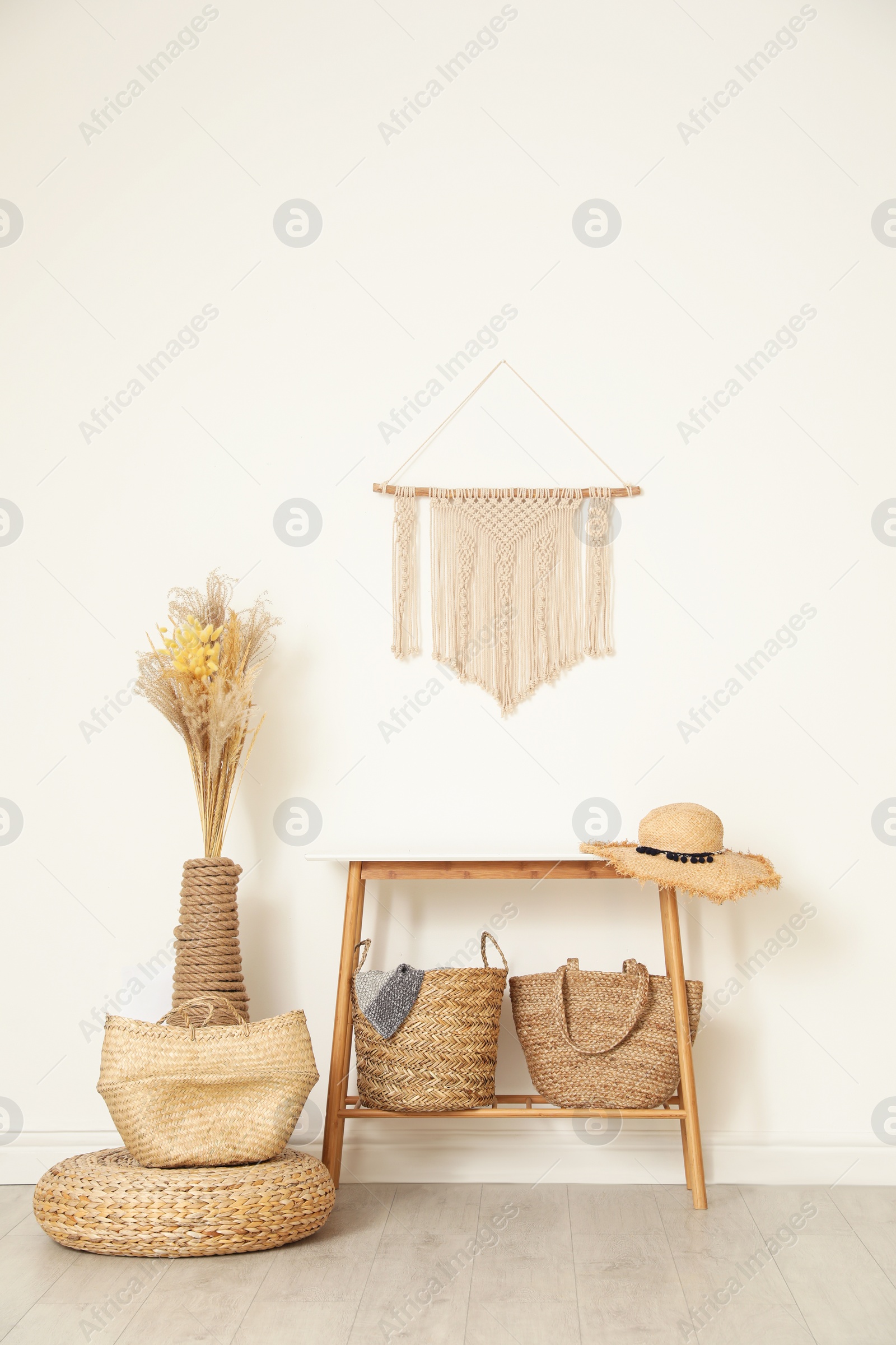 Photo of Stylish room with wooden table and wicker bags near white wall. Interior design