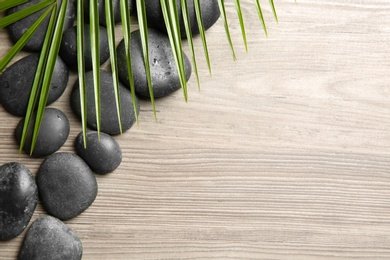 Spa stones with palm leaf on wooden background, top view. Space for text