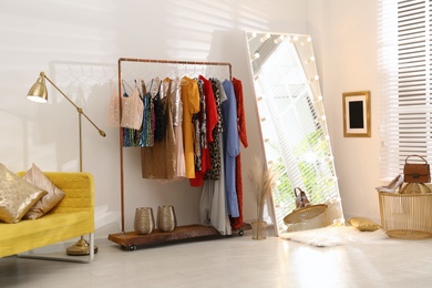 Rack with different stylish women's clothes and mirror indoors