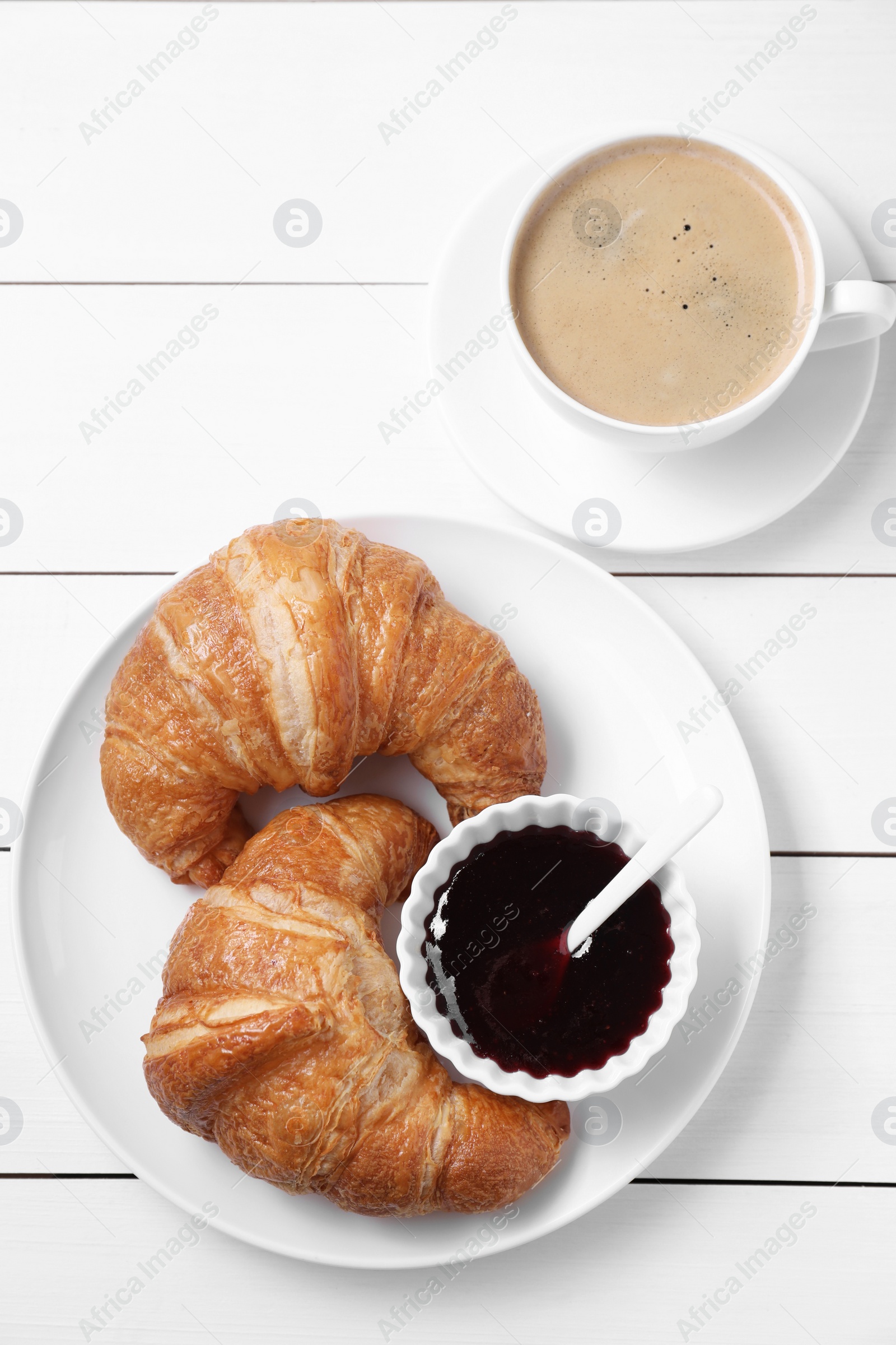 Photo of Fresh croissants, jam and coffee on white wooden table, flat lay. Tasty breakfast