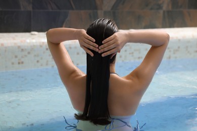 Woman relaxing in spa swimming pool, back view