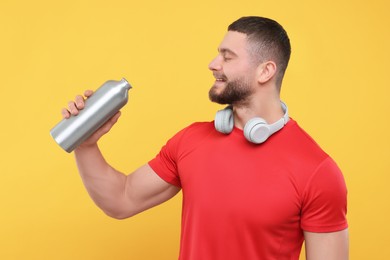 Handsome man with headphones and thermo bottle on yellow background