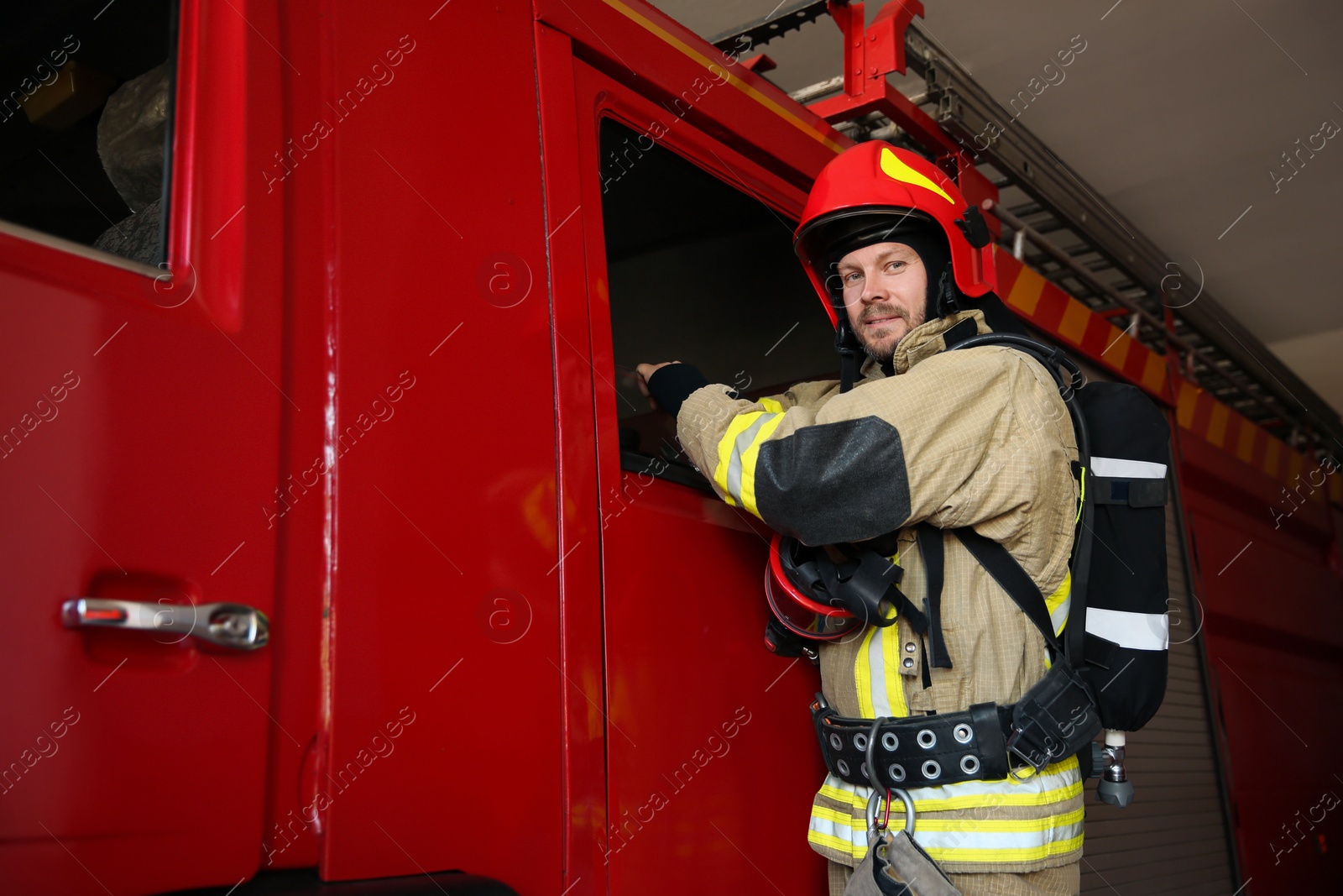 Photo of Portrait of firefighter in uniform near red fire truck at station