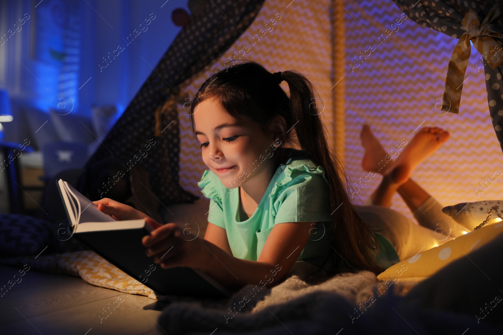 Photo of Little girl reading fairy tale in play tent at home